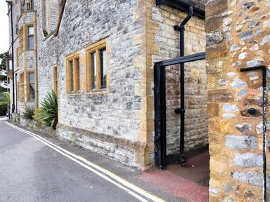 An old stone building with yellow window frames next to a narrow street with double yellow lines