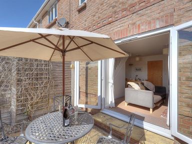 An outdoor patio with metal table and chairs under umbrella and an open door leading to a living room at 1 Coppers Knapp in Lyme Regis