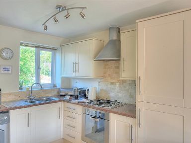 A kitchen with white cabinets a gas stove stainless steel hood and sink at 1 Coppers Knapp in Lyme Regis