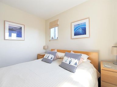 A bedroom with a double bed two bedside tables two lamps two framed pictures on walls and a window at 1 Coppers Knapp in Lyme Regis