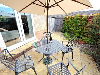 A patio area with a round metal table and four chairs under a large umbrella next to a brick wall and glass doors at 1 Coppers Knapp in Lyme Regis