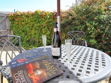 An outdoor metal table with two glasses of prosecco a bottle and a book titled The Last Conquest 1066 at 1 Coppers Knapp in Lyme Regis