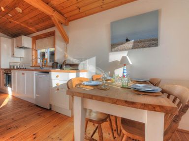 A kitchen with wooden ceiling and floor a dining table with plates and glasses and kitchen appliances at St Anton in Lyme Regis