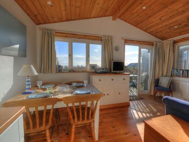 A dining table with chairs set for four near windows and a door leading to a balcony in a wooden ceiling room at St Anton in Lyme Regis