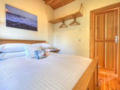 A bedroom with a wooden bed white bedding a wooden door and a wooden shelf with hangers at St Anton Lyme Regis