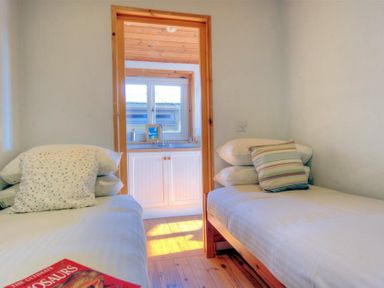 A small bedroom with two single beds and pillows and a view into a kitchen with a sink at St Anton in Lyme Regis