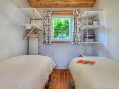 A bedroom with two beds a window in the middle shelves with books and hangers at St Anton in Lyme Regis