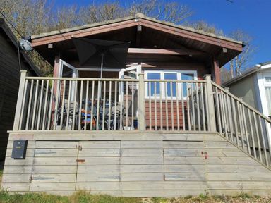 A wooden cabin with a deck railing and patio furniture under an umbrella at St Anton in Lyme Regis