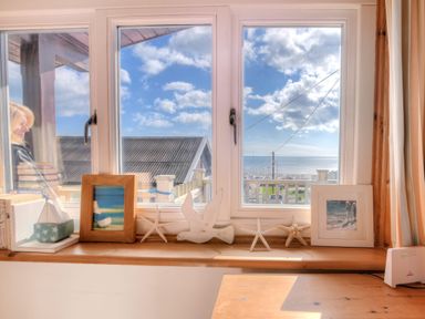 A window sill with starfish, bird decoration, pictures, books, and a small boat with a view of rooftops and the sea at St Anton in Lyme Regis