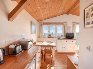 A kitchen and dining area with wooden ceiling and floor a toaster microwave table chairs and a view through the window at St Anton in Lyme Regis