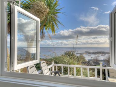 An open window overlooking a balcony with chairs and a view of the sea and boats at The Cabin in Lyme Regis