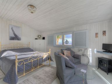 A bedroom with a metal bed, two armchairs, a window with shutters, and a small TV at The Cabin in Lyme Regis