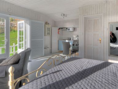 A bedroom with a bed a chair a small kitchen area a door and glass doors leading outside at The Cabin in Lyme Regis