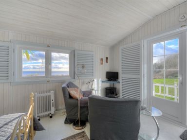 A sitting area with two gray chairs a small TV near two windows and a door leading outside at The Cabin in Lyme Regis