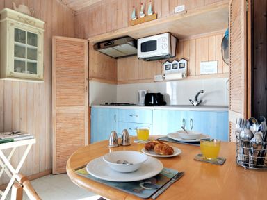 A kitchen with light blue cabinets a microwave toaster kettle and a dining table set with plates glasses and bread at The Cabin in Lyme Regis