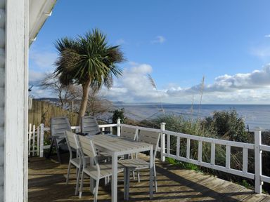 An outdoor deck with table chairs and palm tree overlooking the sea at The Cabin in Lyme Regis