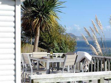 An outdoor deck with a table and chairs with drinks and a blanket overlooking the sea at The Cabin in Lyme Regis