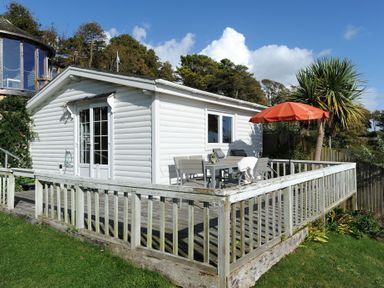 A white cabin with a wooden deck railing and patio furniture with an orange umbrella at The Cabin in Lyme Regis