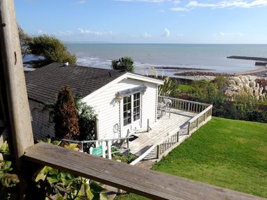 A small white cabin with a wooden deck and lawn overlooking the sea at The Cabin in Lyme Regis