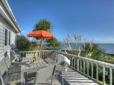 An outdoor wooden deck with a table and chairs an orange umbrella and a view of the ocean at The Cabin in Lyme Regis