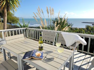 A wooden deck with a table, chairs, wine bottle, glasses, a book, and ocean view at The Cabin in Lyme Regis