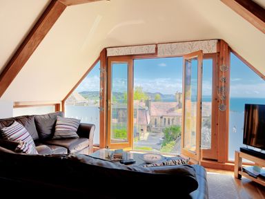 A living room with leather sofas facing a glass coffee table and large windows showing a seaside view at Bucket & Spade Lyme Regis