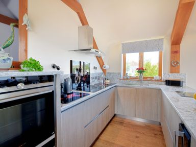 A kitchen with wooden cabinets marble countertops a window with a roller blind and stainless steel appliances at Bucket  Spade Lyme Regis