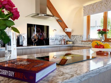A kitchen with a marble countertop and cooktop a cookbook and vegetables on the counter at Bucket & Spade in Lyme Regis