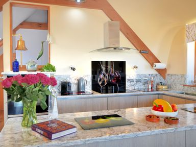 A kitchen with a marble countertop a vase of pink roses a book and a bowl of vegetables at Bucket & Spade Lyme Regis