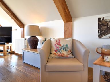 A beige armchair with a decorative pillow next to a wooden side table with a lamp in a living room at Bucket & Spade Lyme Regis