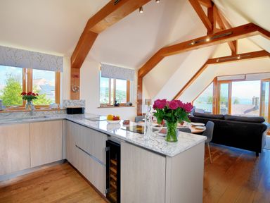 An open kitchen and living area with wooden beams a marble countertop dining table with chairs and a sofa at Bucket & Spade in Lyme Regis
