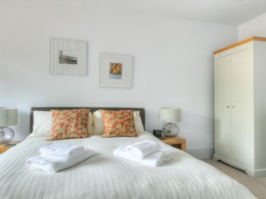 A bedroom with a double bed with red patterned pillows bedside tables with lamps and a white wardrobe at Bucket & Spade in Lyme Regis