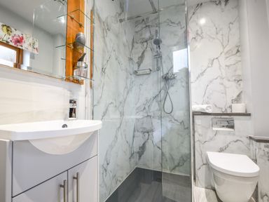 A bathroom with a white sink cabinet a glass shower enclosure and a wall-mounted toilet at Bucket & Spade in Lyme Regis