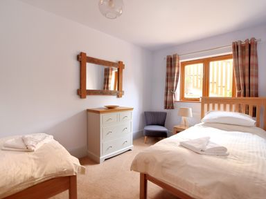 A bedroom with two single beds a chest of drawers a wooden framed mirror a chair and a window with curtains at Bucket & Spade Lyme Regis