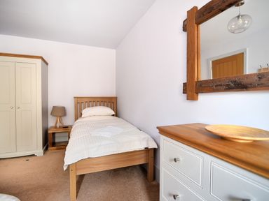 A bedroom with a single wooden bed beige wardrobe bedside table lamp and a chest of drawers with a wooden bowl and mirror at Bucket amp Spade Lyme Regis