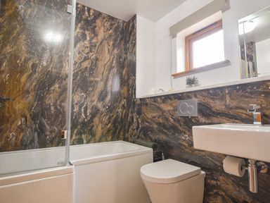 A bathroom with a bathtub shower combination a toilet and a sink with marble wall panels at Bucket amp Spade Lyme Regis