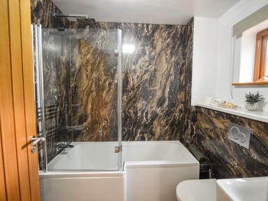 A bathroom with a bathtub shower combination and marble walls at Bucket & Spade Lyme Regis