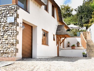 Exterior view of a white building with wooden framed windows and a thatched roof at Bucket & Spade in Lyme Regis