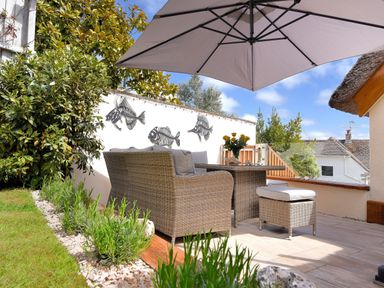 An outdoor patio with wicker furniture an umbrella and wall decorations of fish skeletons at Bucket amp Spade Lyme Regis