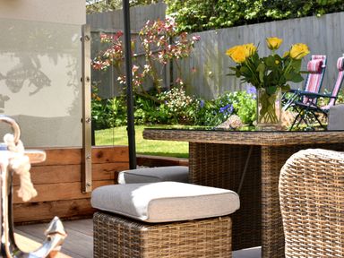 A garden patio with rattan furniture and yellow roses on a glass table at Bucket & Spade in Lyme Regis