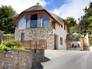 A stone and thatched roof house with large wooden windows and a staircase outside at Bucket & Spade Lyme Regis