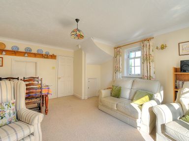A living room with a sofa, armchairs, a dining table with chairs, a bookshelf, and a window with curtains at Blacksmiths Cottage in Lyme Regis