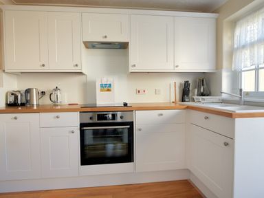 A kitchen with white cabinets wooden countertops an electric oven a kettle toaster and sink at Blacksmiths Cottage in Lyme Regis