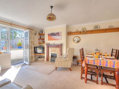 A living room with a fireplace armchair dining table and open door to outside at Blacksmiths Cottage Lyme Regis