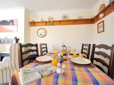 A dining table set with plates glasses of orange juice boiled eggs jar of jam and a newspaper in a room at Blacksmiths Cottage Lyme Regis