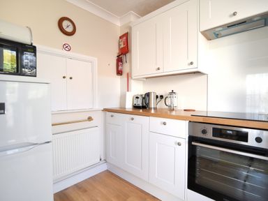 A kitchen with white cabinets wooden countertop oven kettle toaster microwave and fire extinguisher at Blacksmiths Cottage in Lyme Regis
