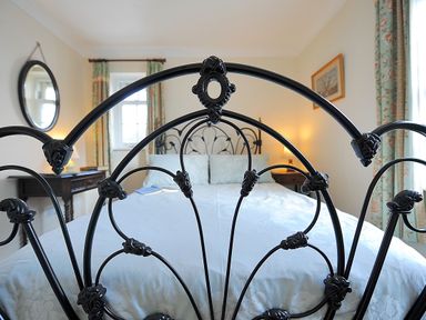 A bedroom with a metal bed frame light blue bedding and curtains beside two table lamps at Blacksmiths Cottage in Lyme Regis
