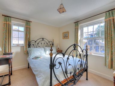 A bedroom with a metal bed frame two windows with curtains and a bedside table at Blacksmiths Cottage in Lyme Regis