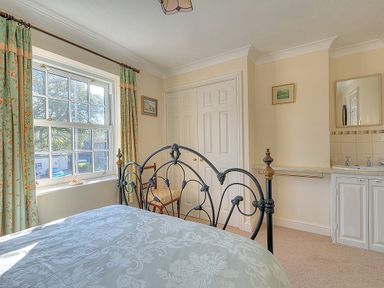A bedroom with a decorative metal bed frame a window with curtains a closet and a sink area at Blacksmiths Cottage in Lyme Regis