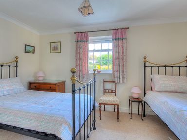 A bedroom with two single beds bedside tables a chair and a window with pink curtains at Blacksmiths Cottage Lyme Regis